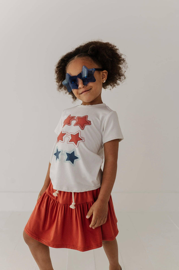 Toddler in star-print tee and red skirt with star-shaped sunglasses, coastal kids fashion