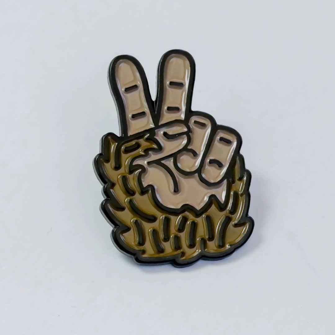 Squatchy enamel pin featuring a furry Bigfoot hand making a peace sign.