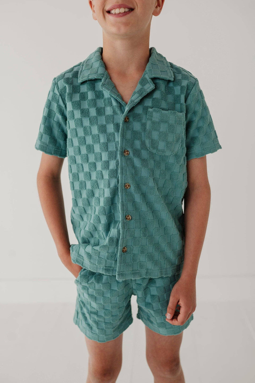 Boy in teal checkered short-sleeve pajama set with button front and chest pocket