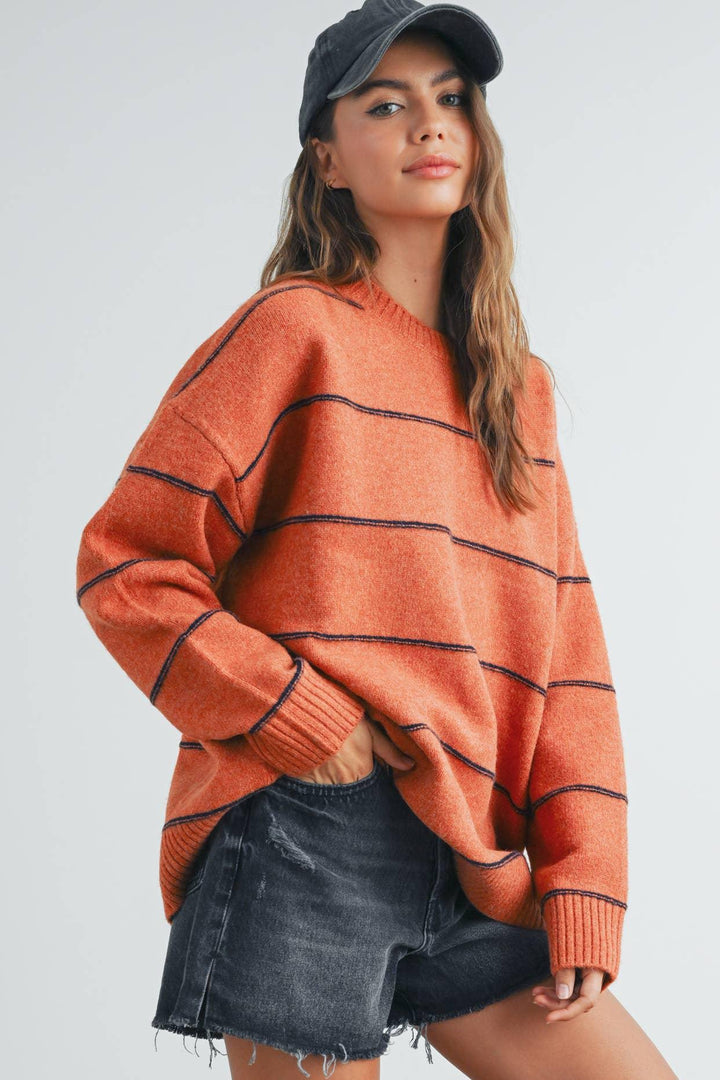 Woman in orange striped sweater, black denim shorts, and baseball cap