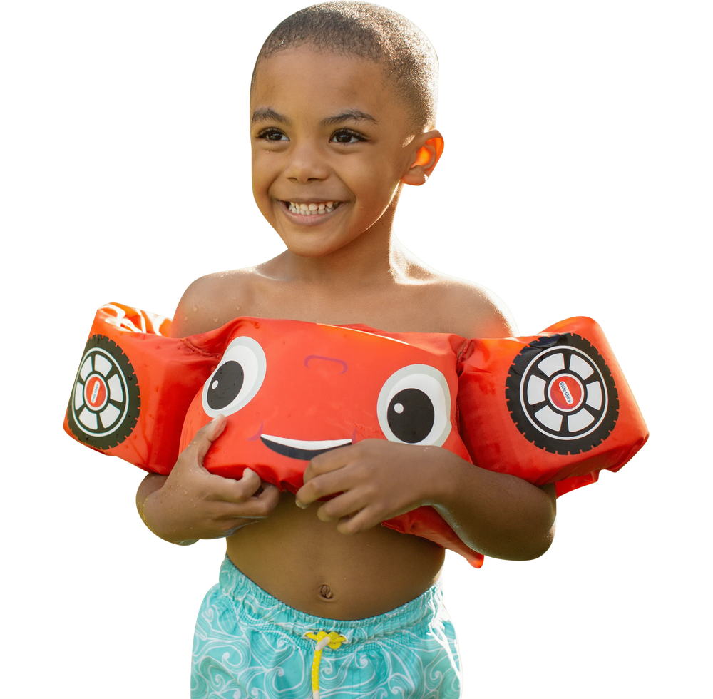 A smiling child wearing a PoolCandy Little Tikes Cozy Coupe red car floatie vest.