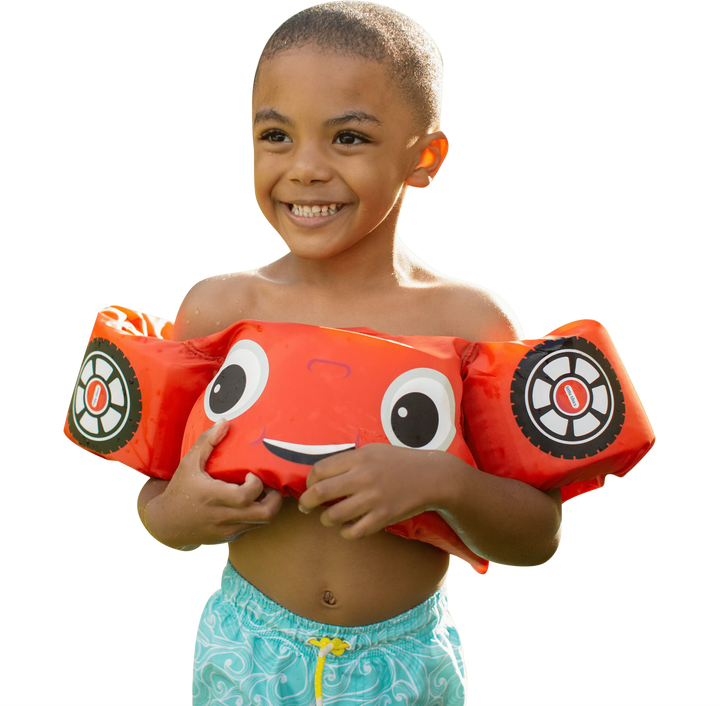 A smiling child wearing a PoolCandy Little Tikes Cozy Coupe red car floatie vest.