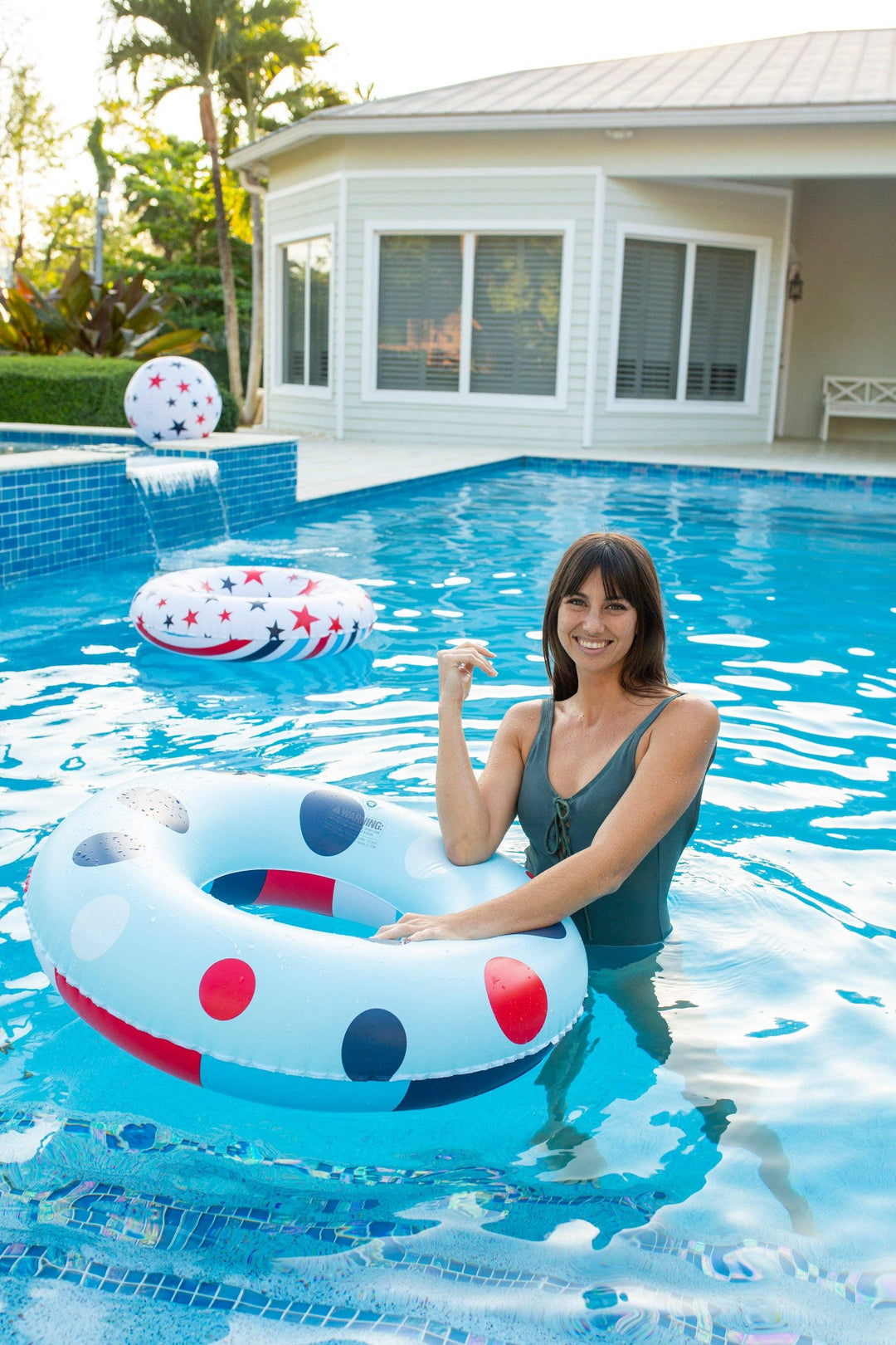 Woman smiling in pool with red, white, and blue polka dot inflatable ring, perfect for summer pool days and outdoor fun.