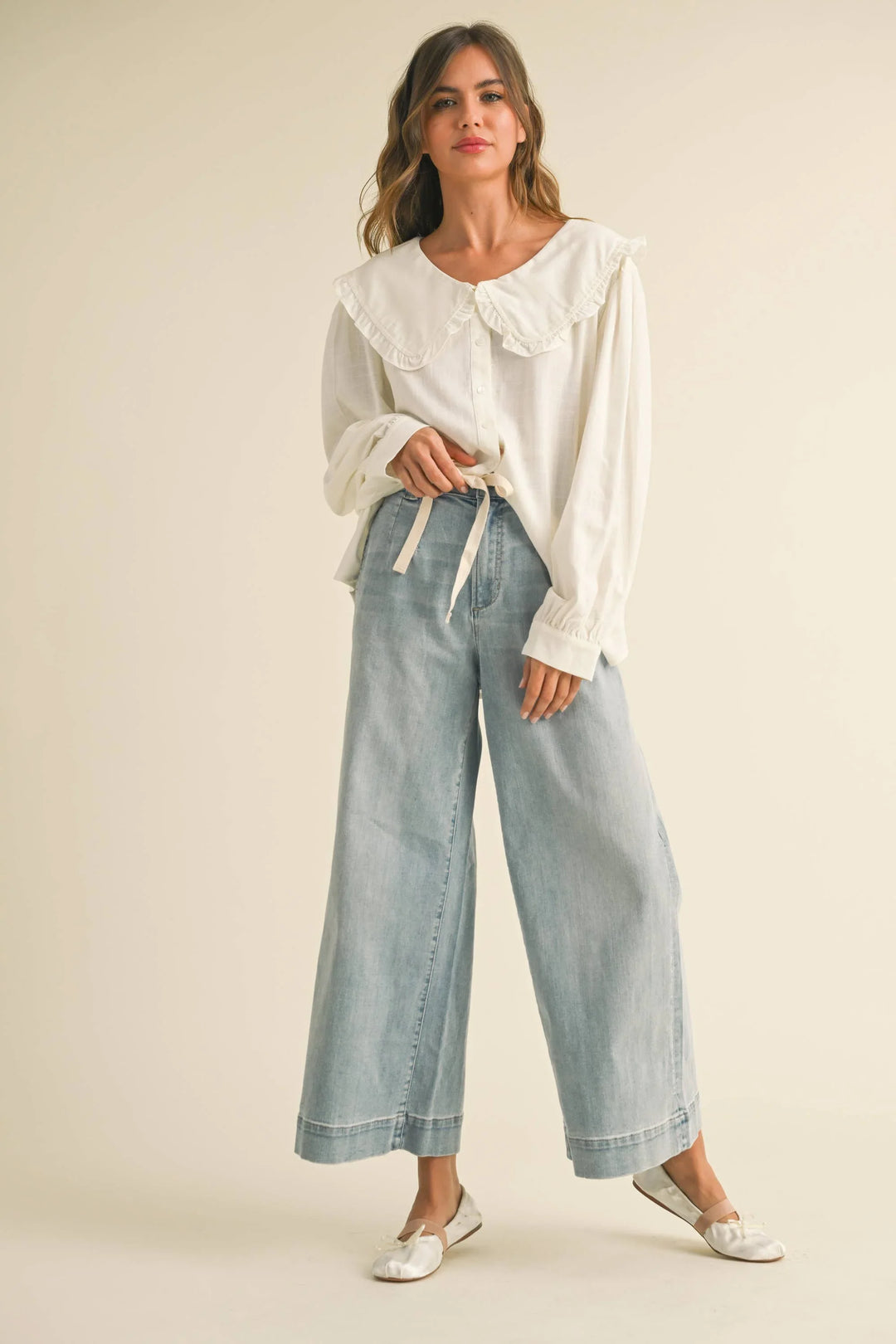 Woman in white ruffle blouse and light wash wide-leg jeans, coastal style outfit