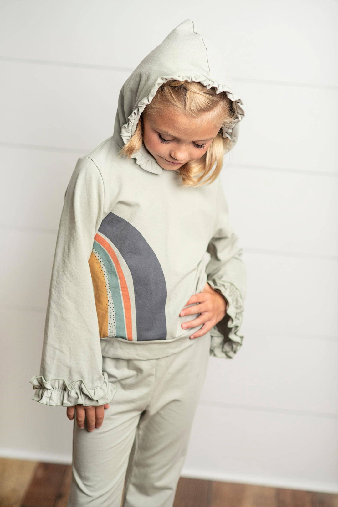 Girl wearing a gray sage Oopsie Daisy rainbow hooded sweatsuit lounge set