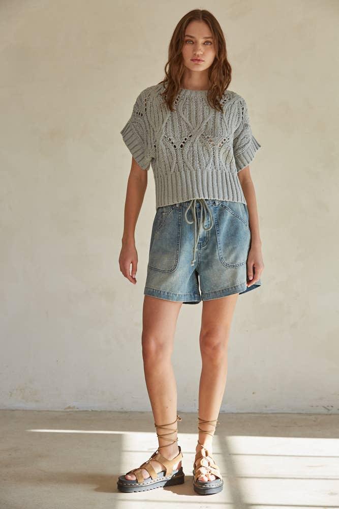 Woman wearing gray knit crop top, denim shorts, and lace-up sandals for casual summer style