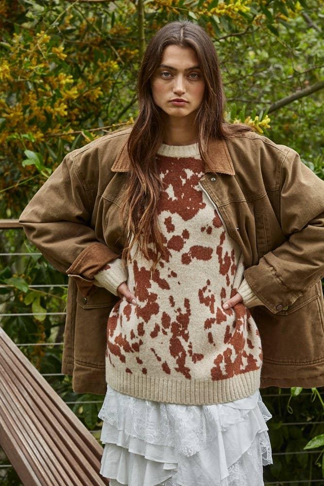 Woman in cozy cow print sweater, brown jacket, and white ruffle skirt outdoors