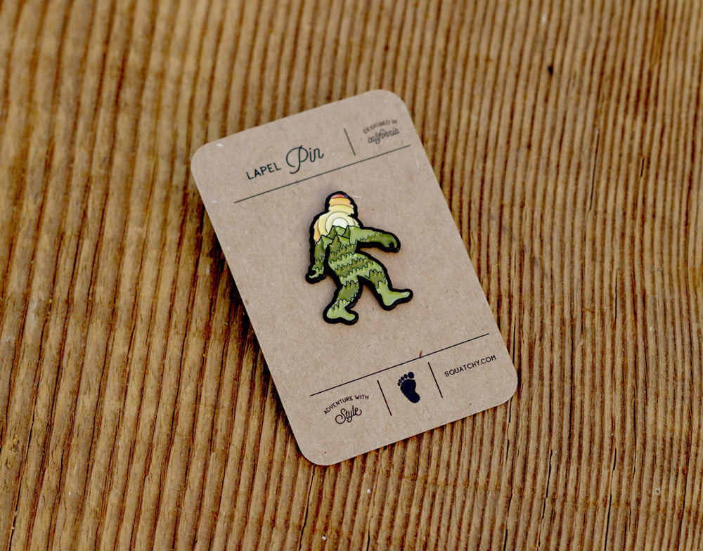 Green Sasquatch lapel pin on rustic wood, designed in California, adventure with style