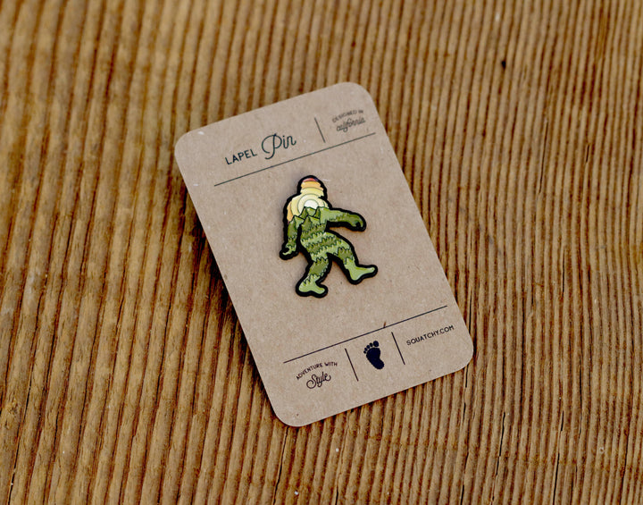 Green Sasquatch lapel pin on rustic wood, designed in California, adventure with style