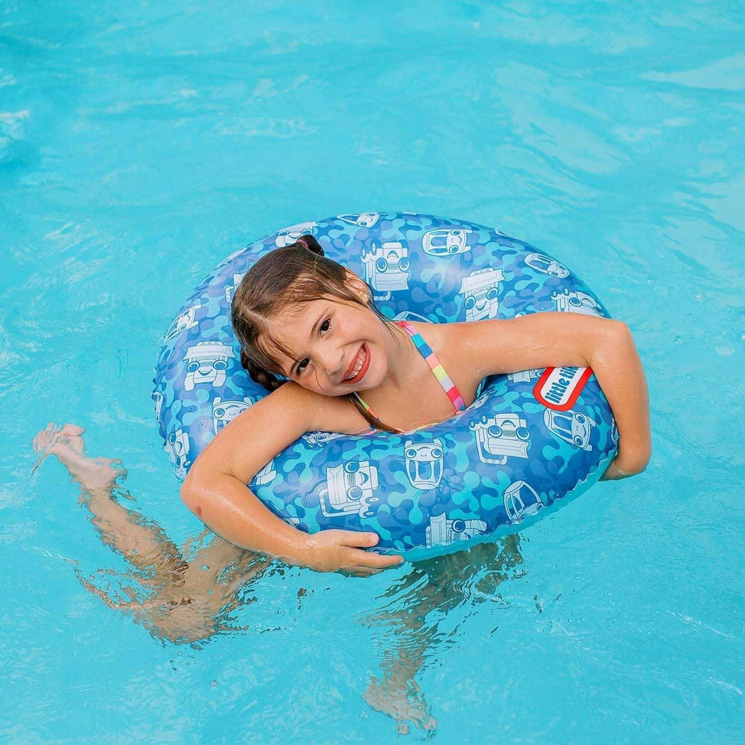 Child smiling in blue pool float with car patterns, enjoying summer swim fun