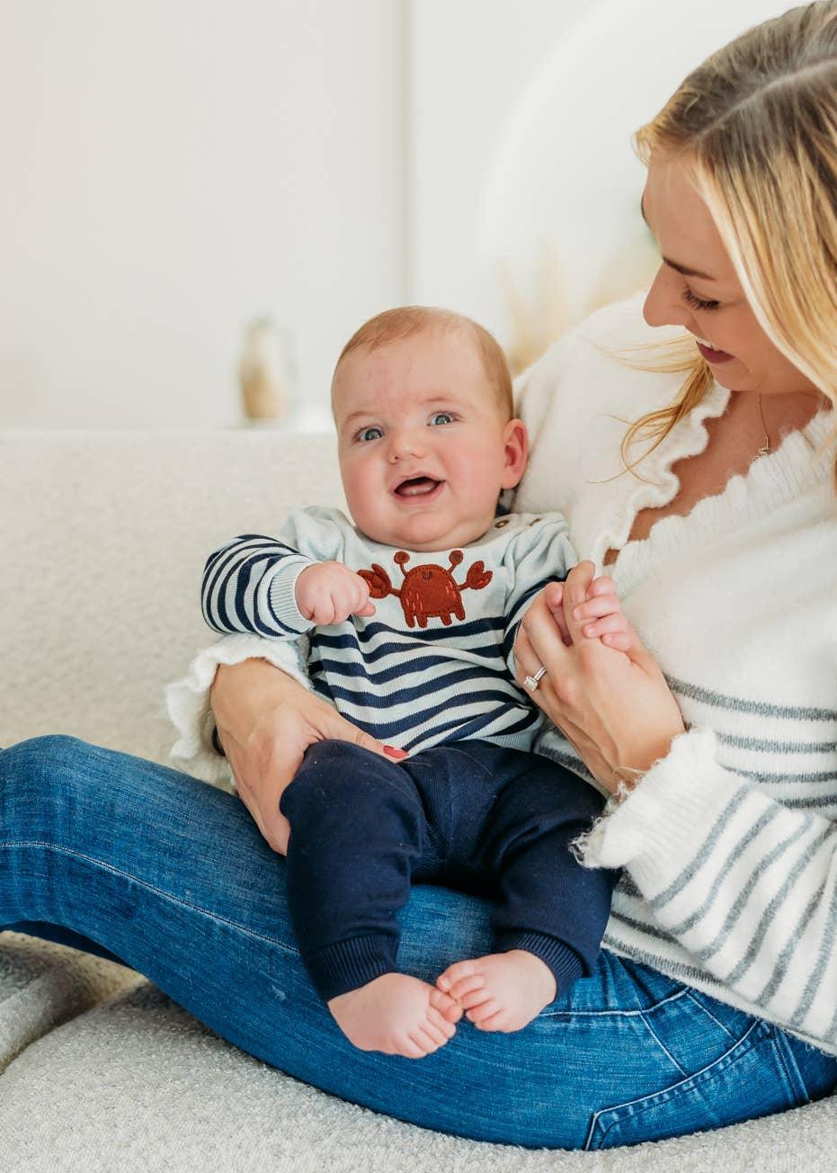 Baby in crab-themed striped outfit held by mom on couch