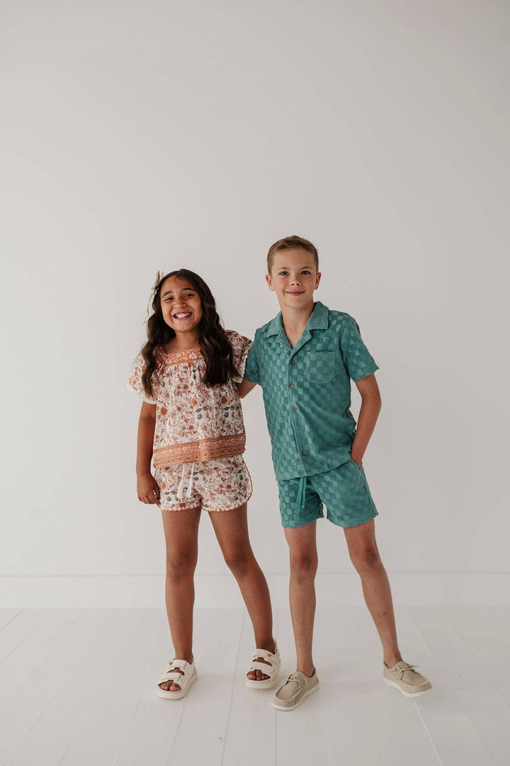 Kids in matching coastal-style outfits, floral top with shorts and teal checkered shirt set, perfect for PNW adventures.