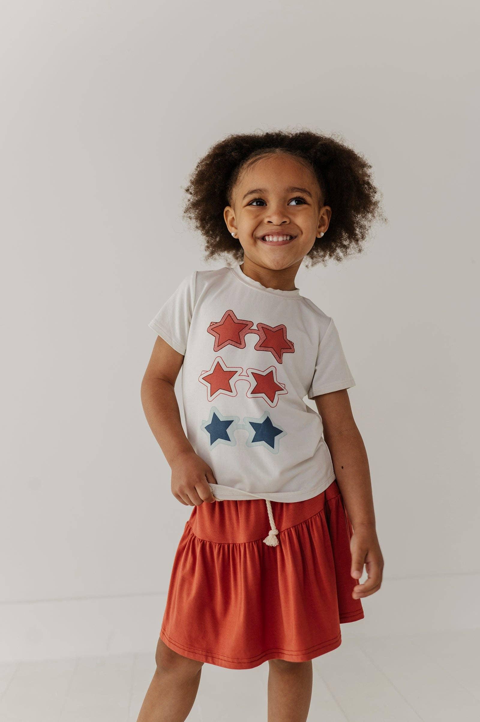 Toddler girl in white star-print tee and rust skirt, coastal PNW style