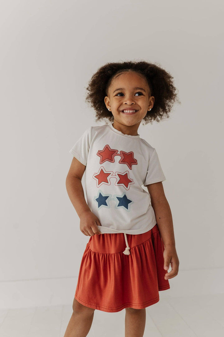 Toddler girl in white star-print tee and rust skirt, coastal PNW style