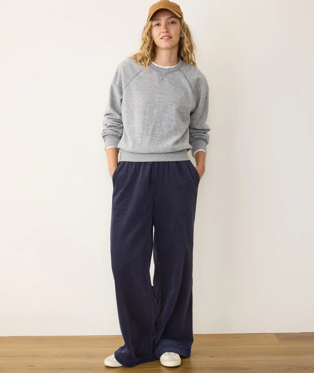 Woman in gray sweatshirt, navy corduroy pants, and tan cap for casual coastal style