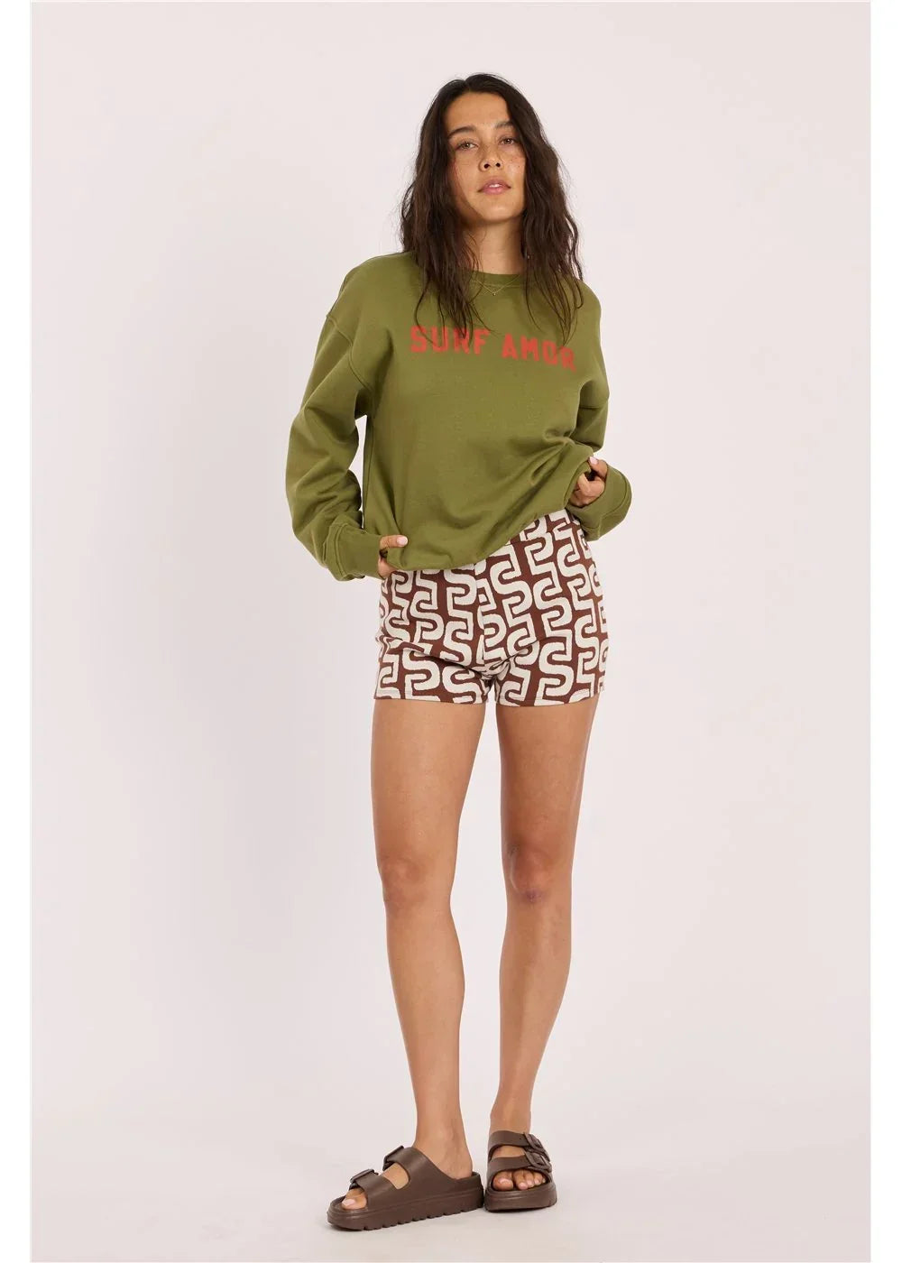 Olive green 'Surf Amor' sweatshirt with patterned shorts and sandals, coastal lifestyle outfit