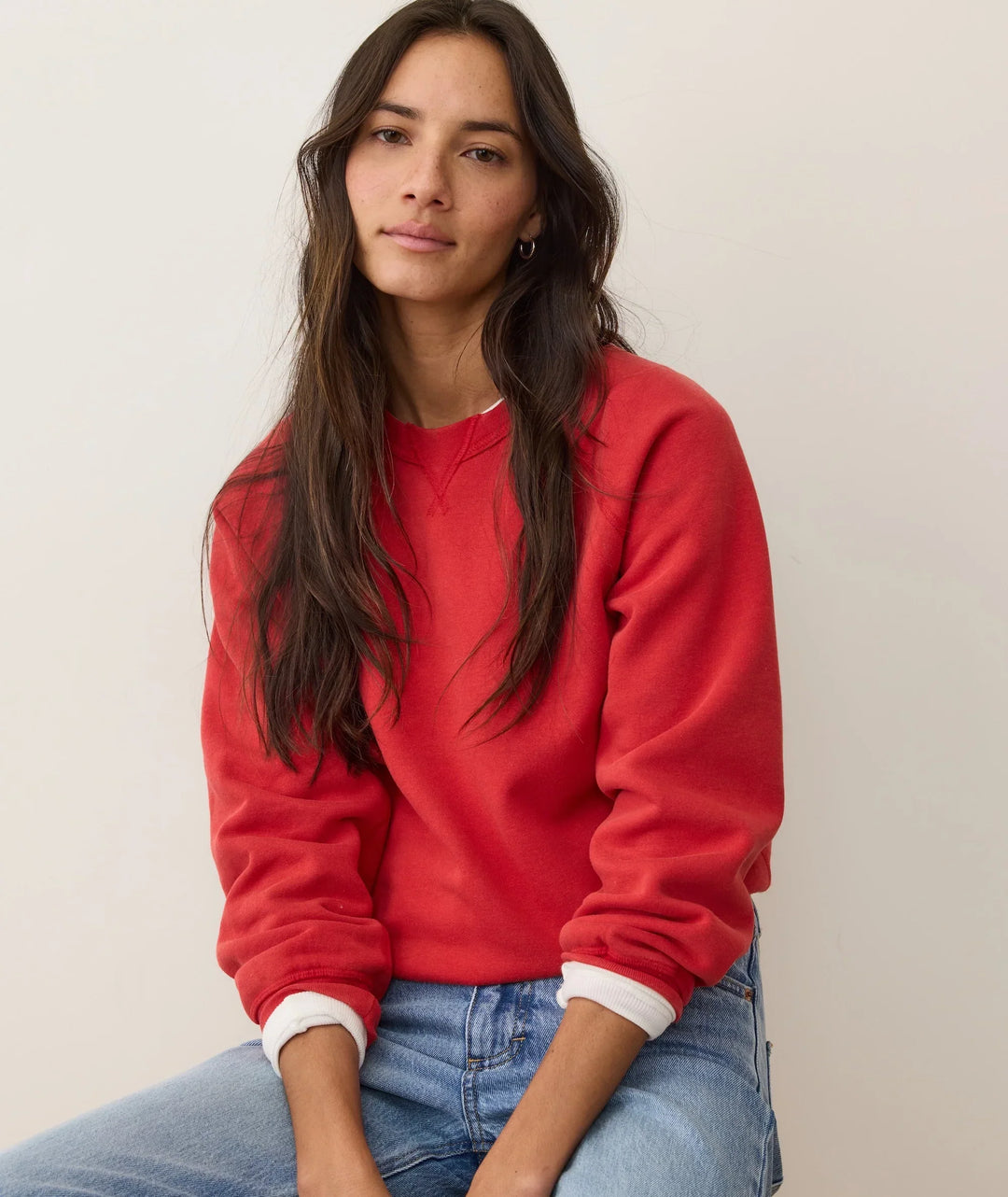 Woman in red crewneck sweatshirt with white cuffs, paired with blue jeans, casual coastal style