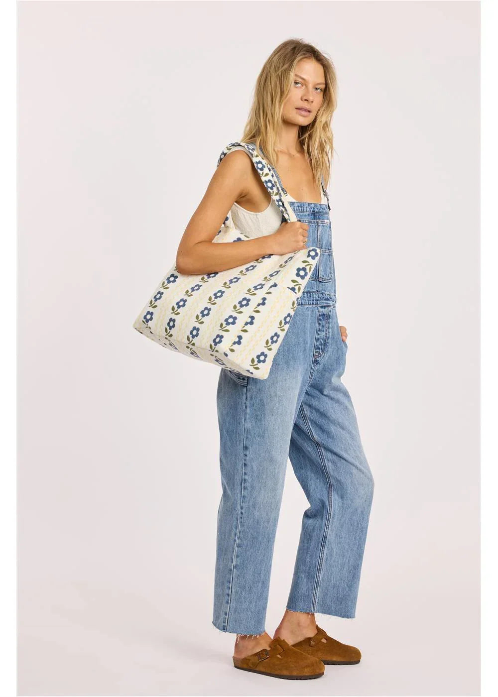 Woman in denim overalls carrying floral tote bag, coastal style for beach days and bike rides