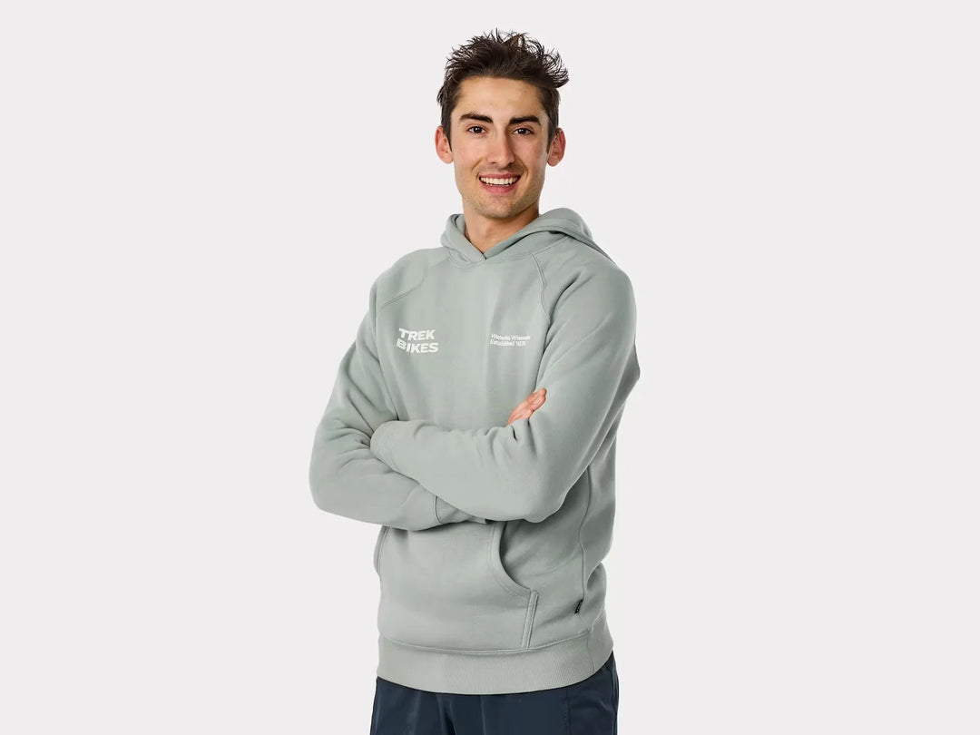 Man wearing light green Trek Bikes hoodie, arms crossed, smiling against white background