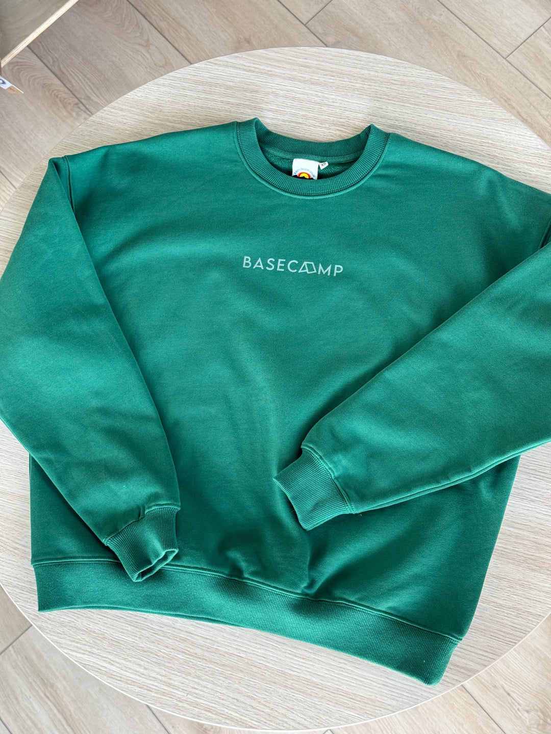 Green Basecamp sweatshirt with logo, laid on wooden table for outdoor lifestyle gear