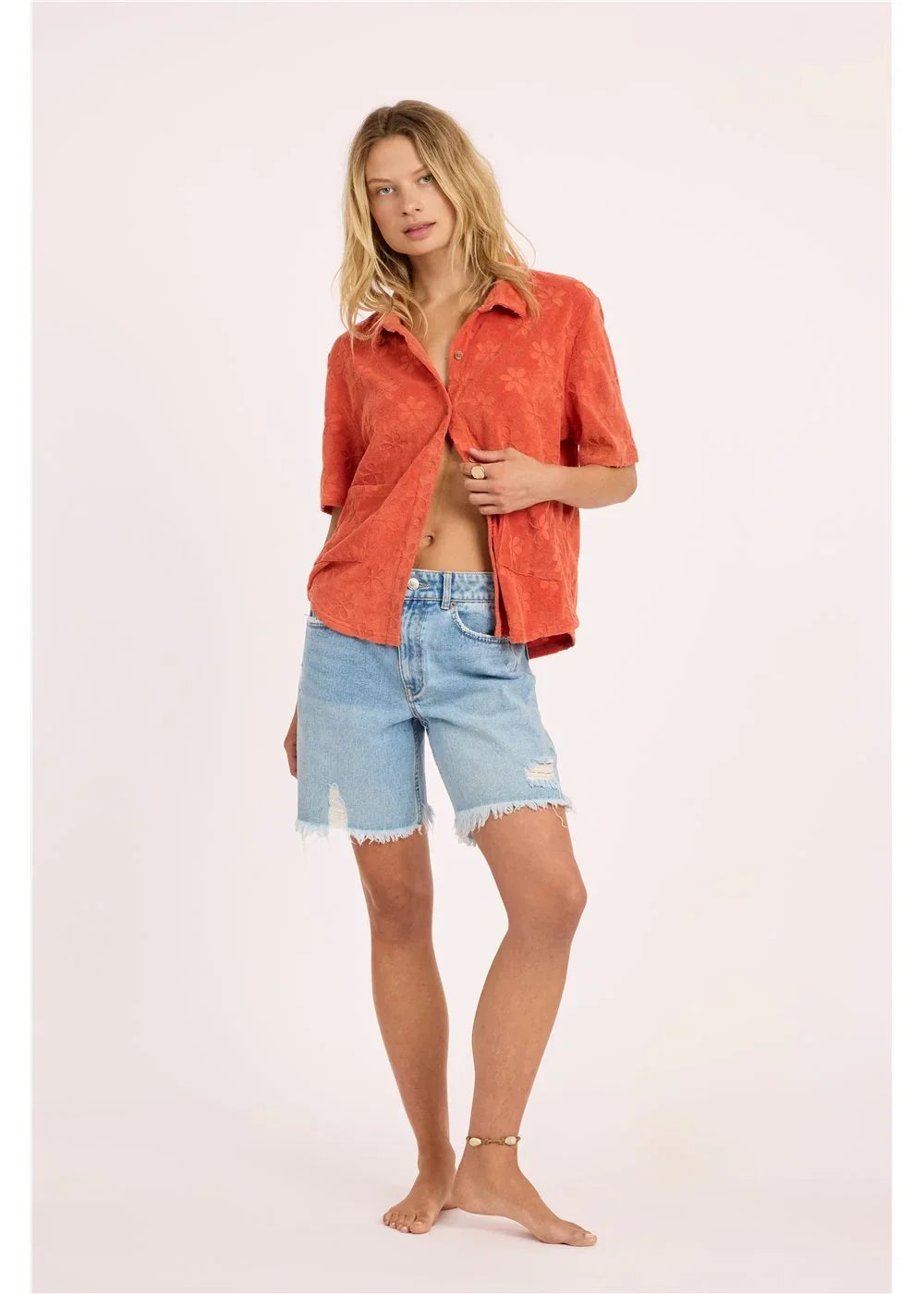 Woman in coral floral shirt and distressed denim shorts, coastal outdoor style