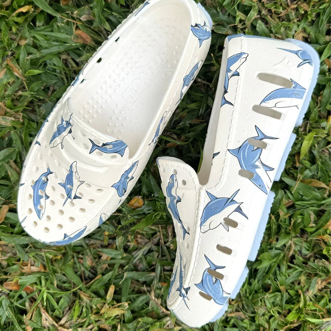 White shark-print clog sandals on grass, perfect for beach or poolside adventures.