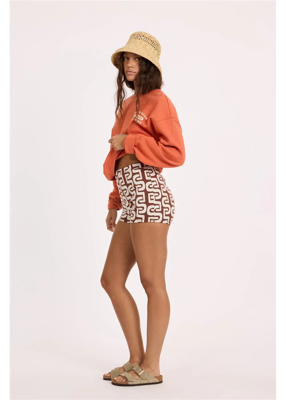 Woman in orange cropped sweatshirt, patterned shorts, straw hat, and sandals for coastal PNW style