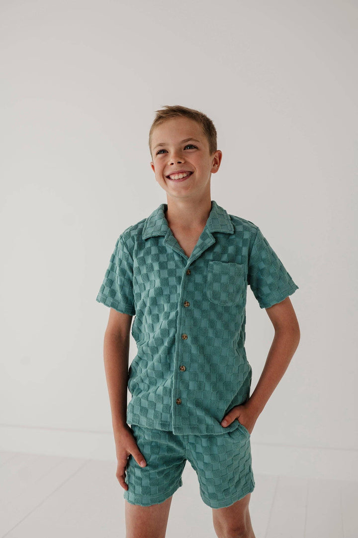 Boy in teal checkered short sleeve pajama set with button front and chest pocket