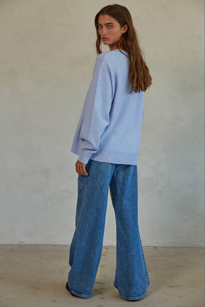 Woman in light blue sweater and wide-leg denim jeans, coastal style outfit