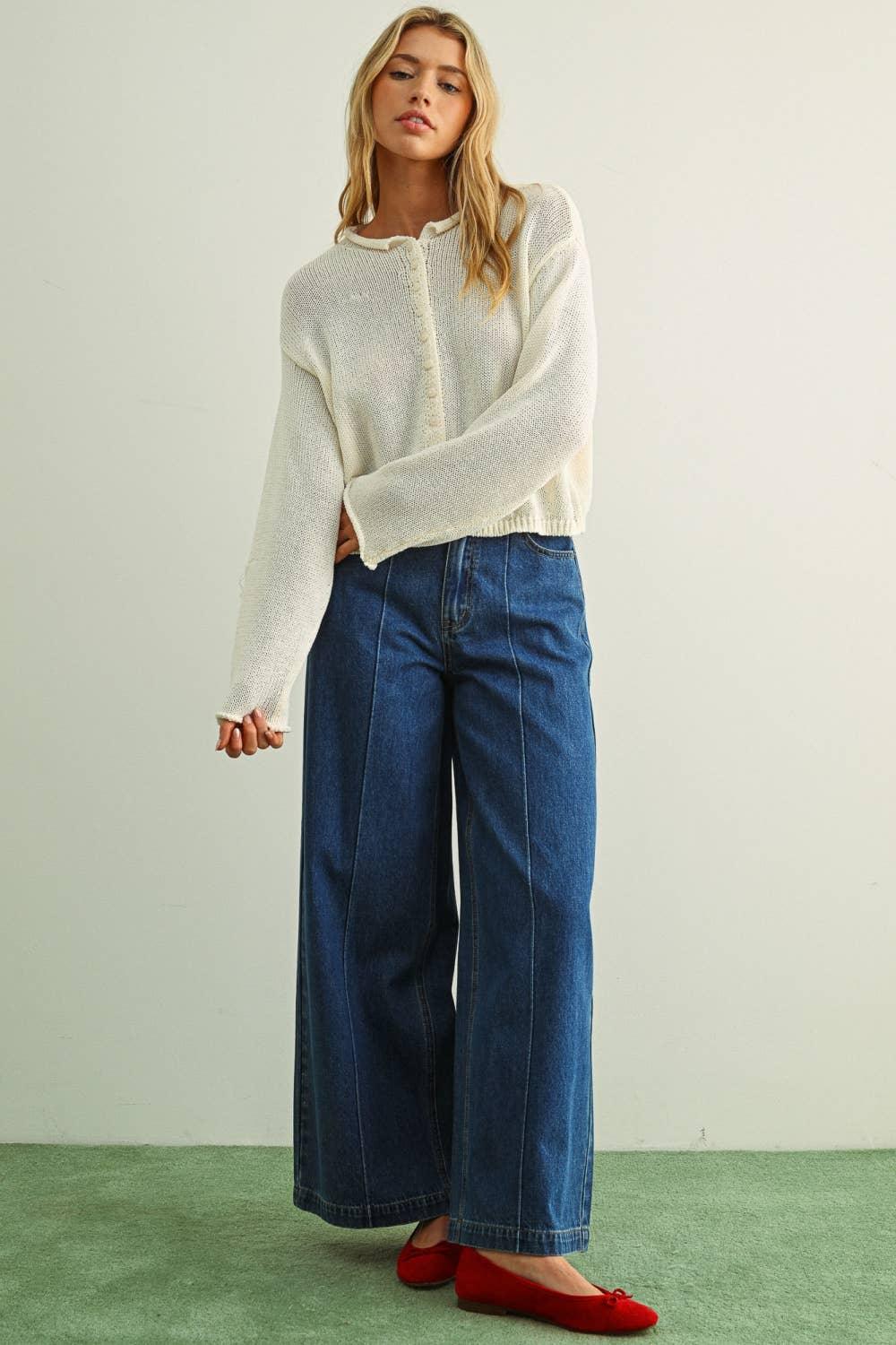 Woman in cream knit cardigan, wide-leg denim jeans, and red flats