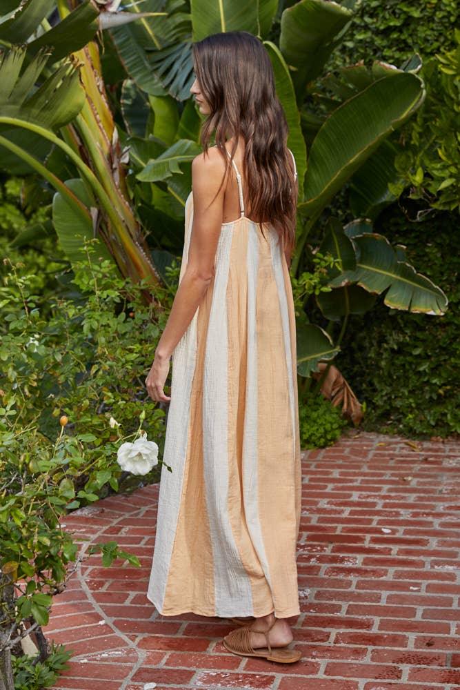 Woman in striped maxi dress walking on brick path near tropical plants, coastal style outfit