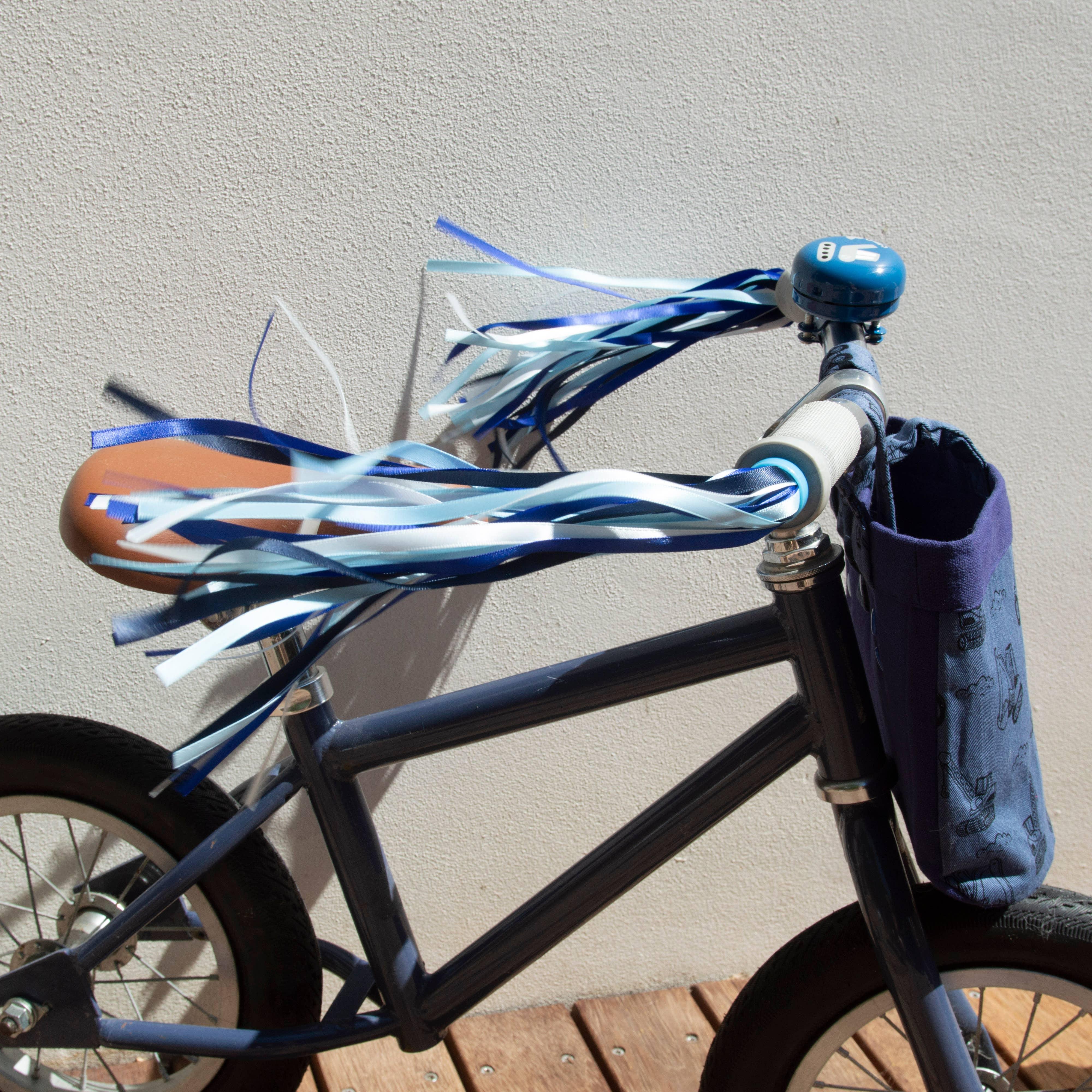 Kids bike with blue and white streamers, bell, and front basket on wooden deck