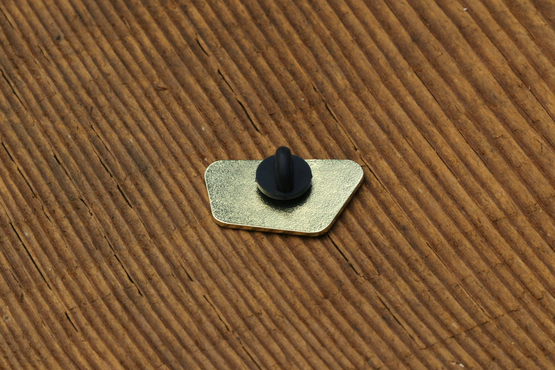 Back view of a Squatchy enamel pin showing the metal post and black rubber clutch on cardboard.