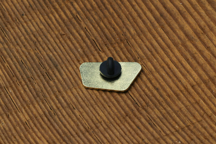 Back view of a Squatchy enamel pin showing the metal post and black rubber clutch on cardboard.