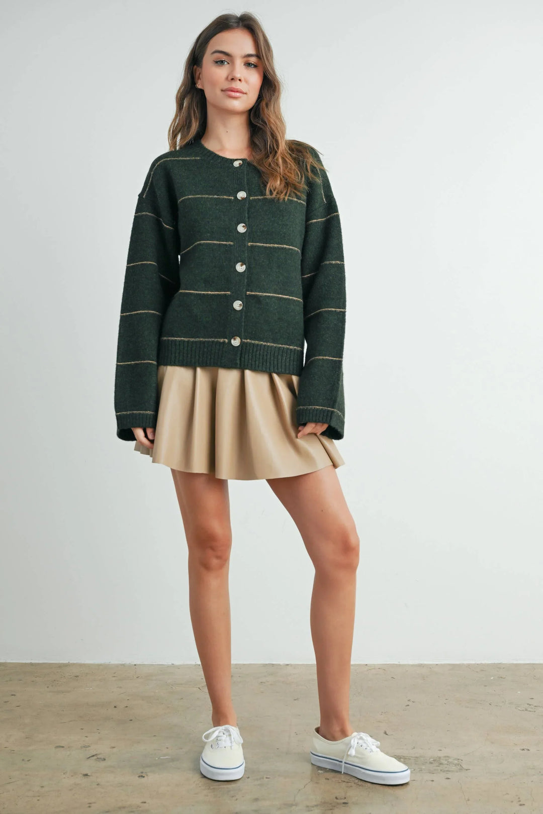 Woman in green striped cardigan, beige pleated skirt, and white sneakers for casual coastal style