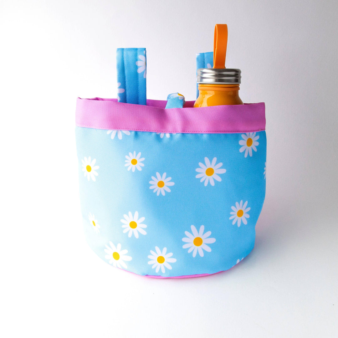 Blue daisy print bike basket with pink trim holding orange water bottle, perfect for beach days and bike rides