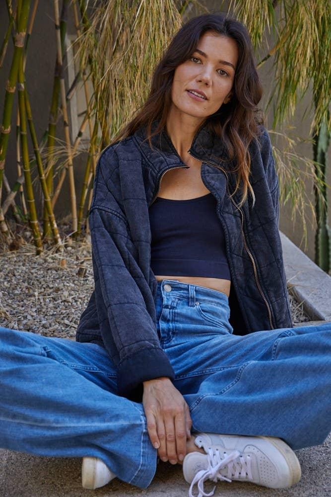 Woman in quilted jacket, crop top, and wide-leg jeans sitting outdoors near bamboo