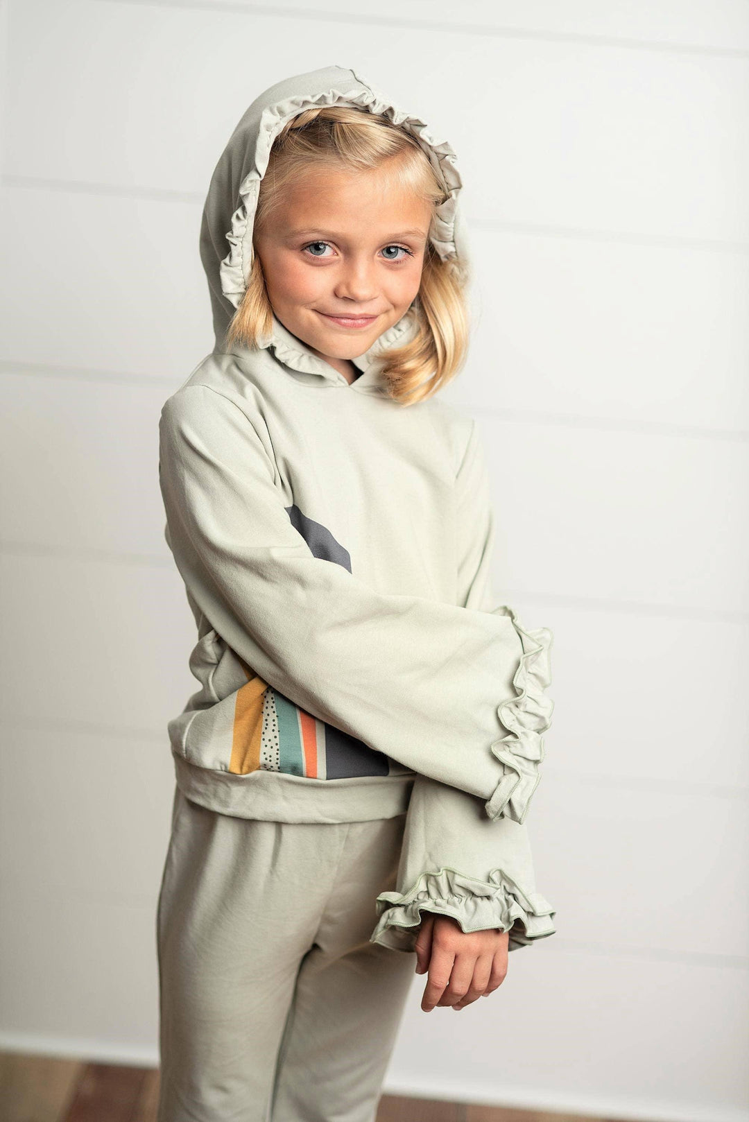 Girl wearing an Oopsie Daisy gray sage rainbow hooded sweatsuit lounge set.