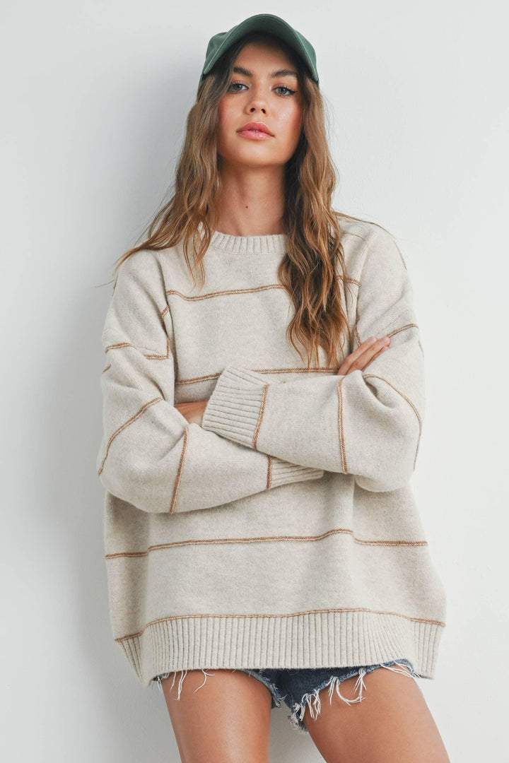 Woman in cozy cream sweater with tan stripes, green cap, and denim shorts