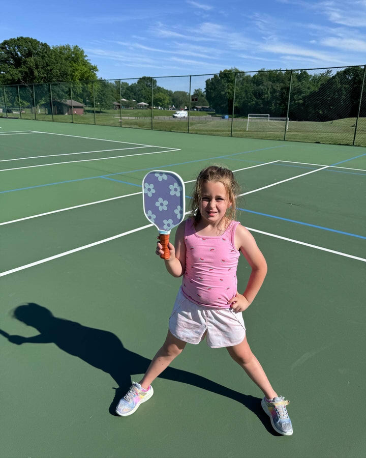 Girl holding floral pickleball paddle on green court, ready to play outdoors