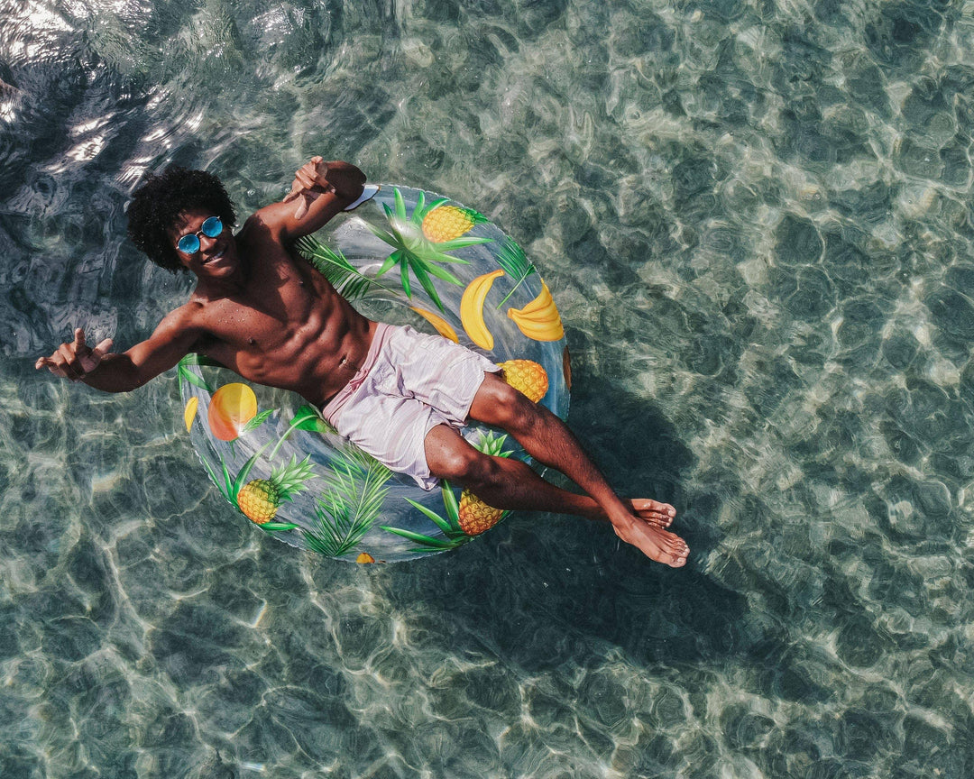 Man floating on tropical fruit pool float in clear water, beach day vibes