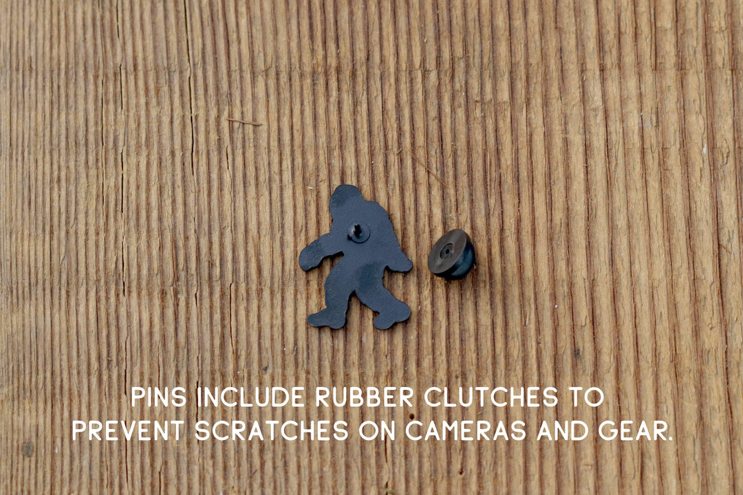 Black Bigfoot-shaped pin with rubber clutch for camera gear protection on wood