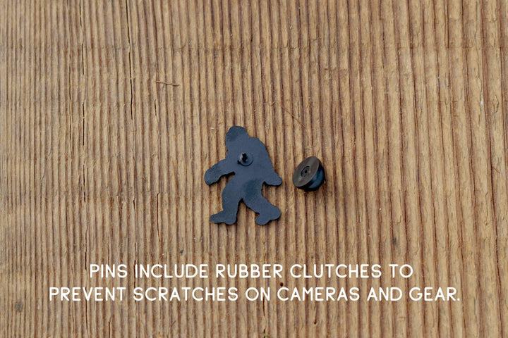 Black Bigfoot-shaped pin with rubber clutch for camera gear protection on wood
