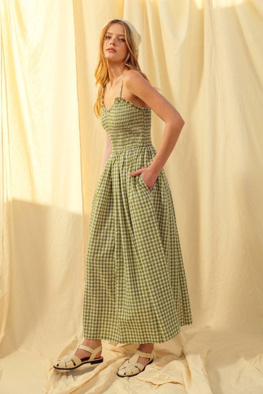 Green gingham midi dress with smocked bodice, thin straps, and side pockets, paired with cream sandals