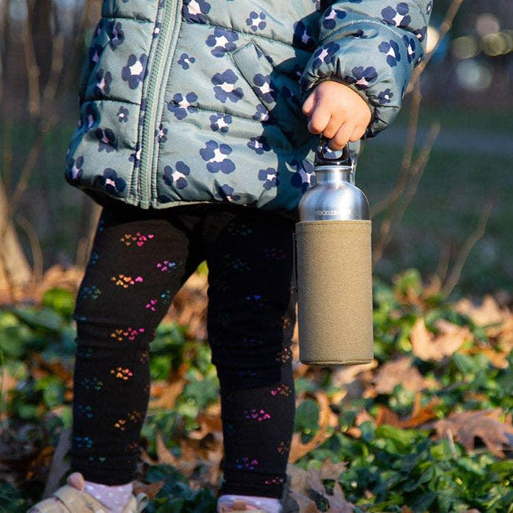Child holding stainless steel water bottle with cozy sleeve, outdoors in fall leaves
