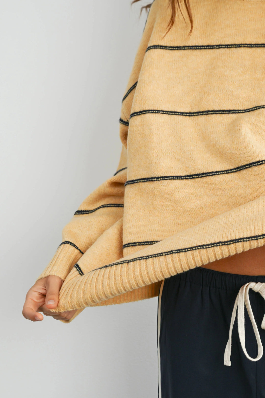 Mustard yellow ribbed knit sweater with black contrast stitching, paired with navy drawstring pants for coastal style.