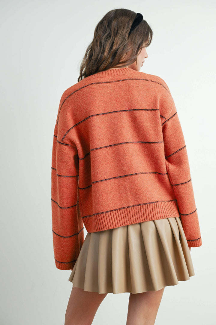 Rust orange striped knit sweater with black lines, paired with beige pleated skirt, coastal style outfit