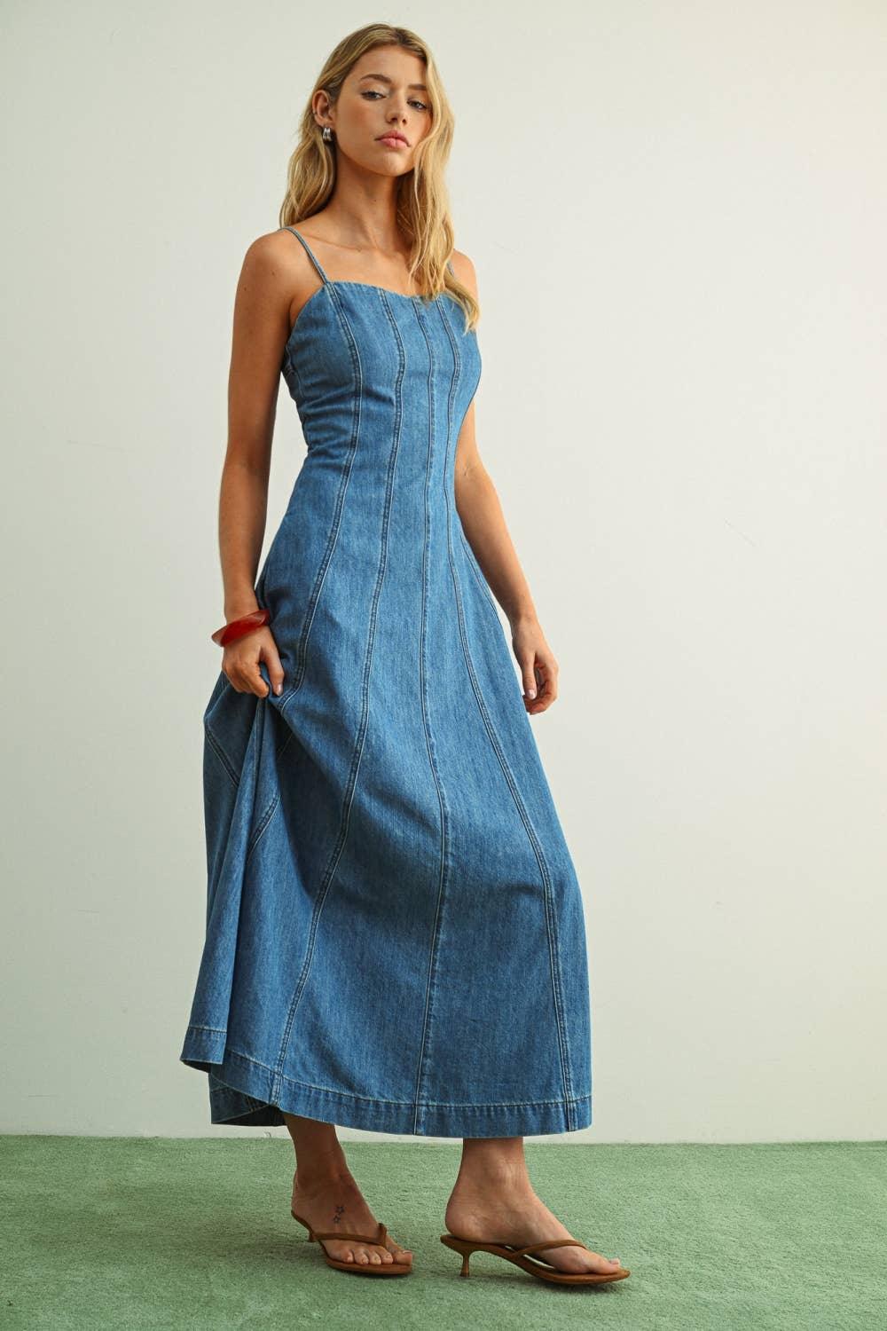 Woman in blue denim midi dress with thin straps, standing on green floor, wearing brown heeled sandals