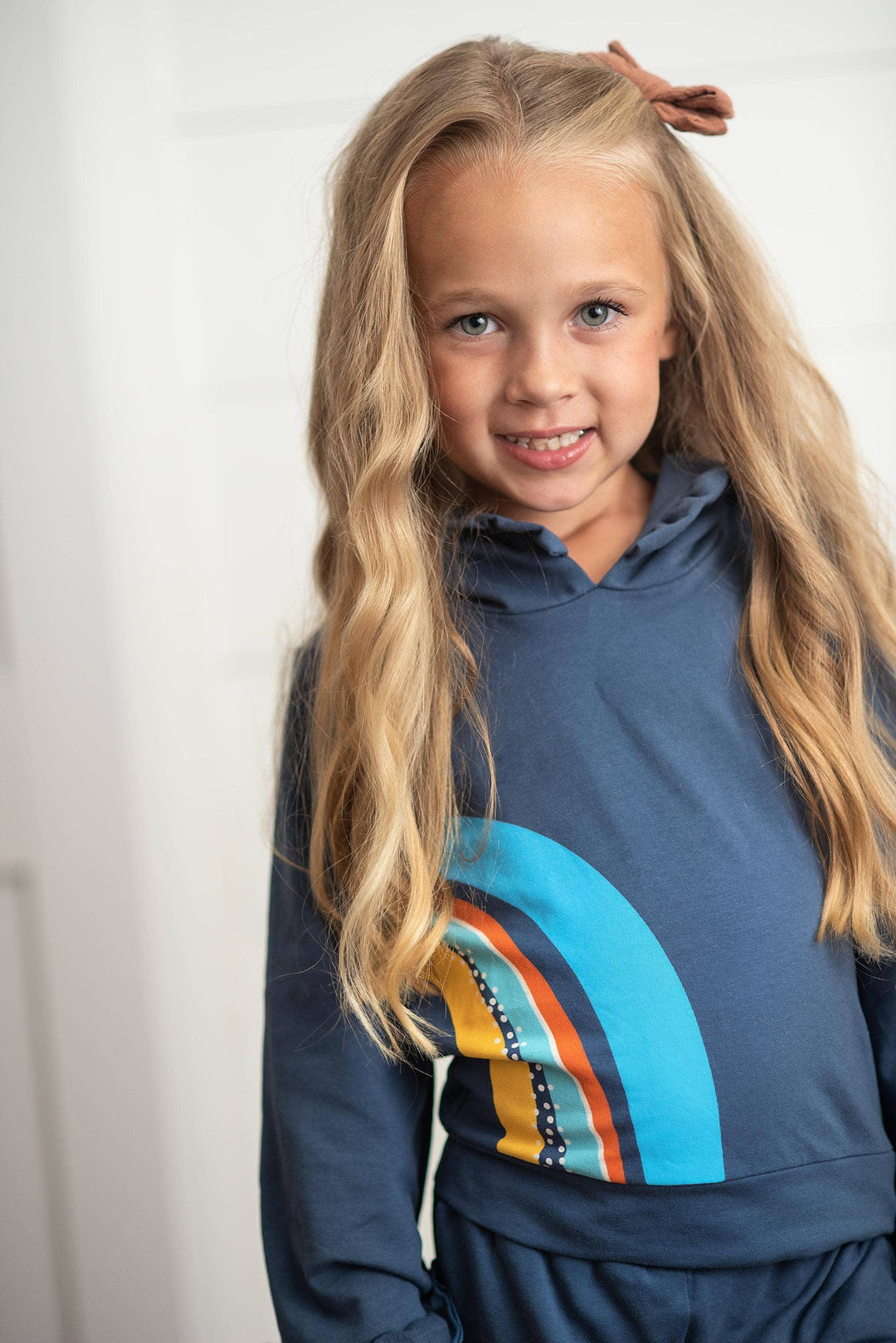 Girl in navy hoodie with rainbow graphic, coastal style kids apparel