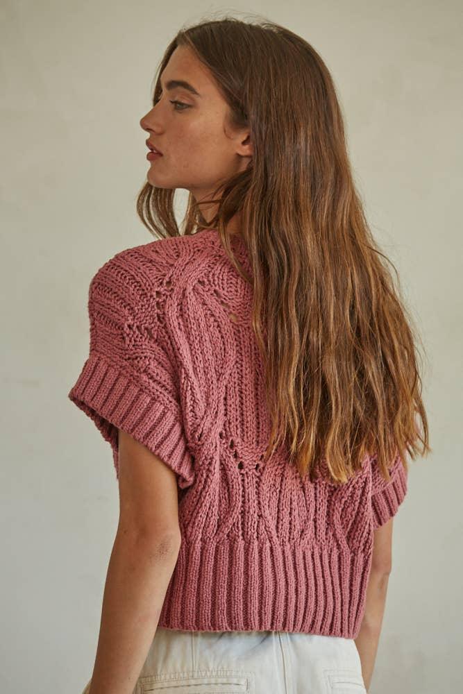 Pink knitted crop top with cable knit pattern and short sleeves, worn by woman with long hair